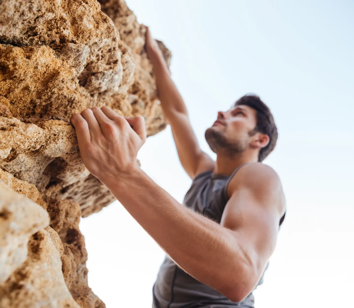 young brunette man climbing natural rocky wall utc