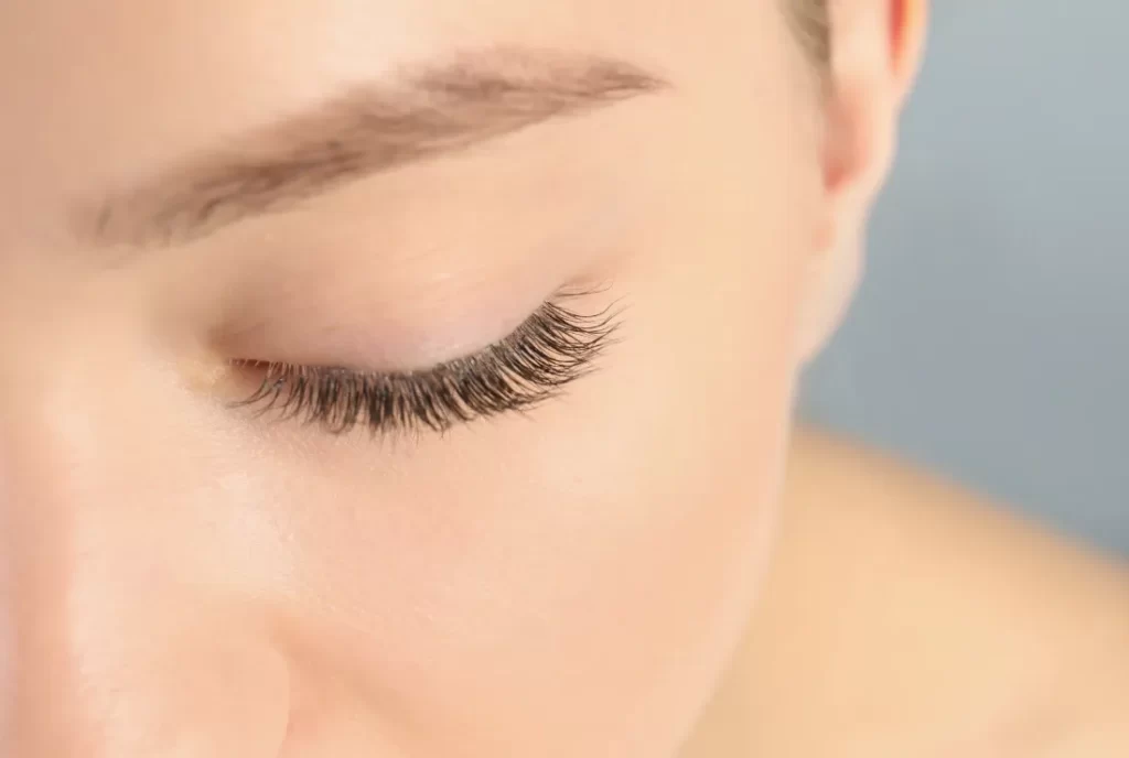 young woman with beautiful long eyelashes on gray utc